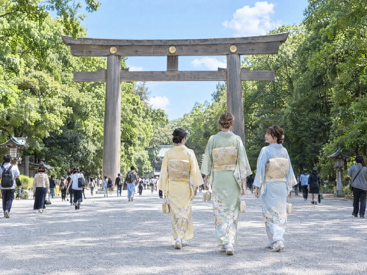 Three friends in pale yellow, pale green and light blue houmongi walking along the gravel approach toward the great torii gate of Meiji Shrine, seen from behind